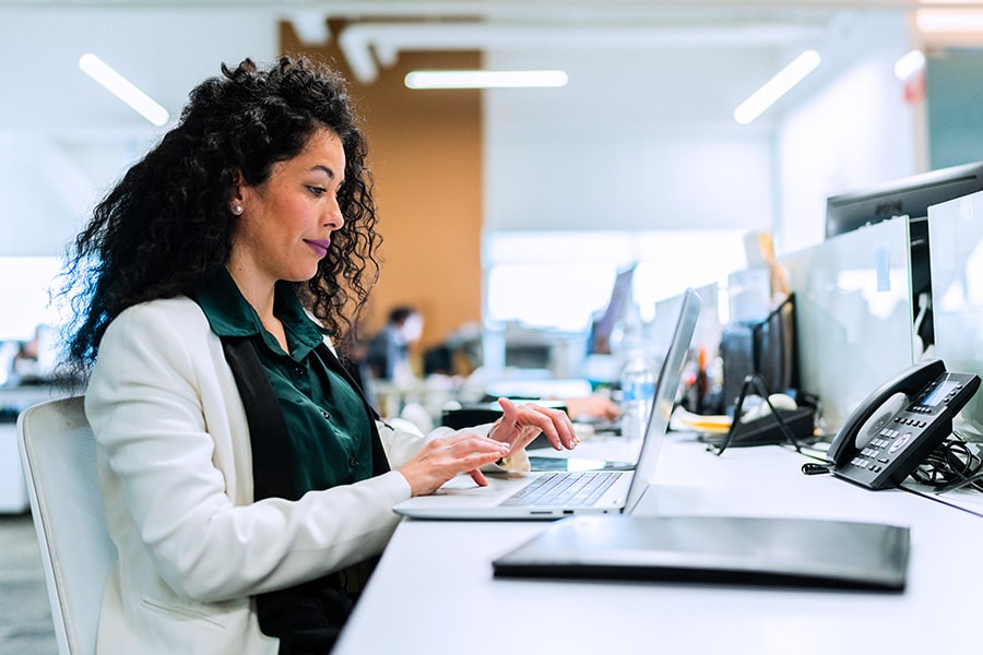 A professional woman with curly hair working on a laptop in a modern office setting