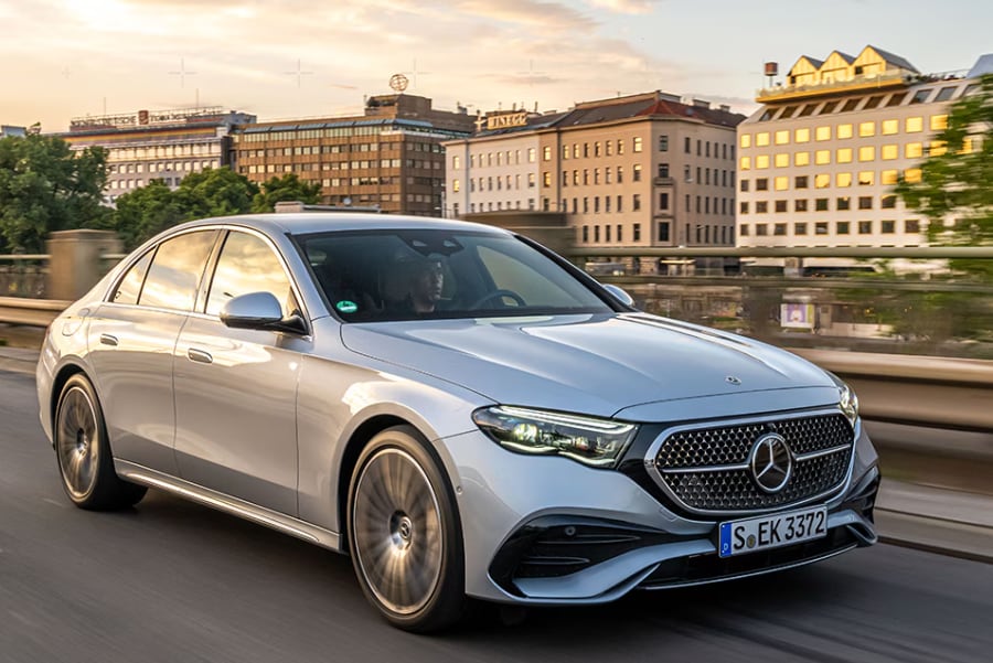 Luxury sedan driving through a city at sunset.